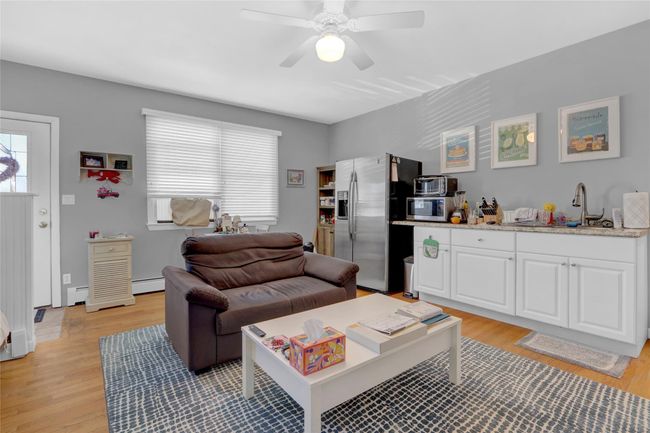 Living room featuring light wood-type flooring, baseboard heating, ceiling fan, and sink | Image 20