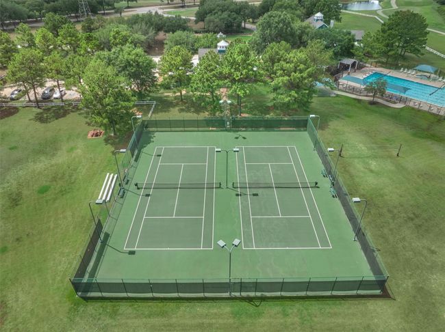 This photo showcases a recreational area featuring two tennis courts surrounded by greenery. Adjacent to the courts is a swimming pool, providing a great space for outdoor activities and relaxation. | Image 38