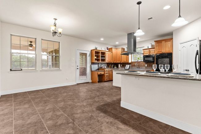 Kitchen with tasteful backsplash, island exhaust hood, open shelves, visible vents, and black appliances | Image 8