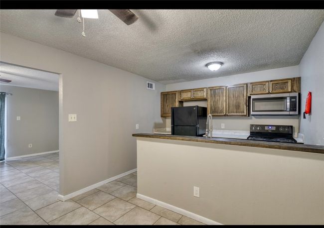 Kitchen with black appliances, ceiling fan, light tile patterned flooring, a textured ceiling, and dark countertops | Image 16