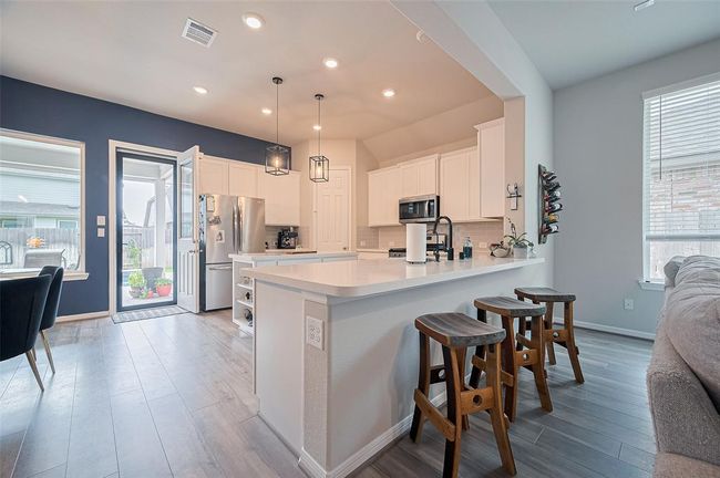Open kitchen with bar stool seating, island kitchen with shelving and stainless steel appliances. | Image 21