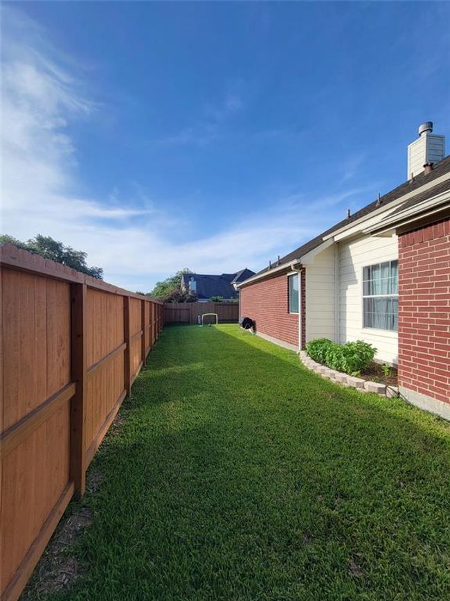 This photo showcases a side yard with a well-maintained lawn, bordered by a wooden fence on one side and a brick house on the other. The space is open and bright, ideal for outdoor activities or gardening. | Image 33
