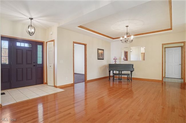 Entryway featuring a tray ceiling, light wood-type flooring, baseboards, and an inviting chandelier | Image 12