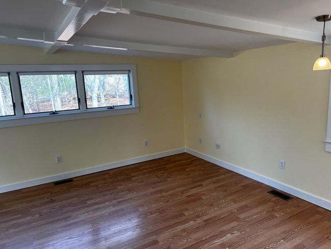 Empty room with dark wood-style floors, baseboards, visible vents, and beamed ceiling | Image 4