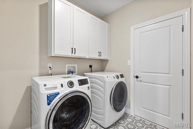 Washroom with cabinet space, independent washer and dryer, light tile patterned floors, and baseboards | Image 17