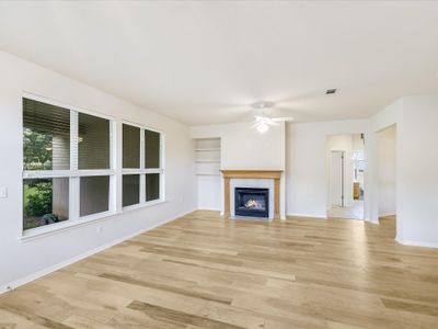 The living room has gorgeous wood floors and a gas fireplace. The room looks out to the lovely backyard with a park like setting. | Image 3