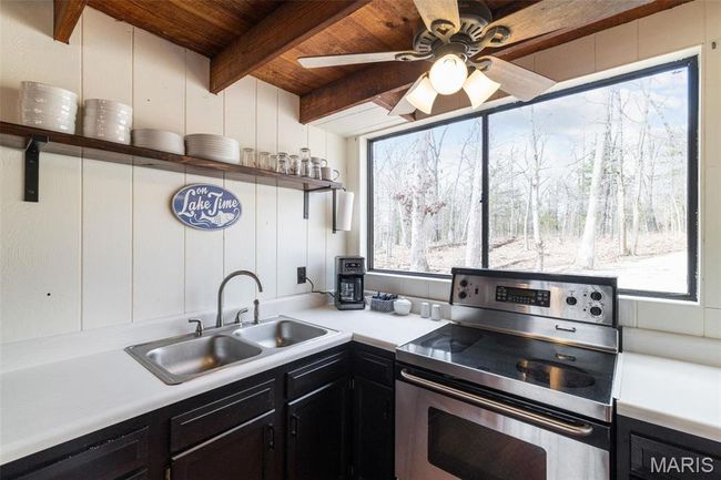 Kitchen featuring electric range, beam ceiling, open shelves, a sink, and dark cabinetry | Image 19