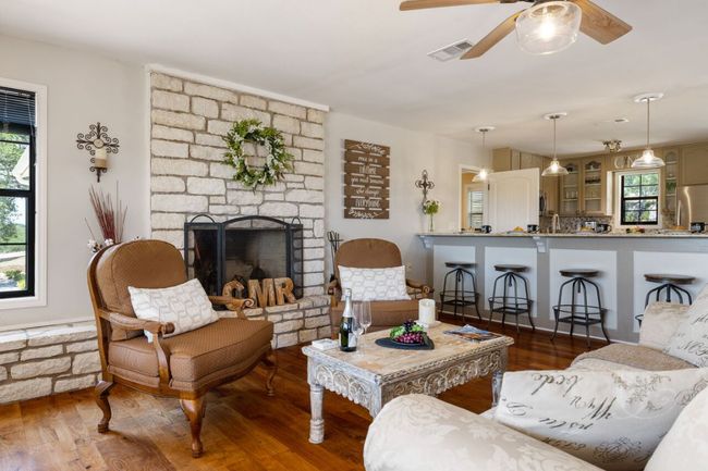 Living room featuring a ceiling fan, wood finished floors, healthy amount of natural light, and a stone fireplace | Image 15