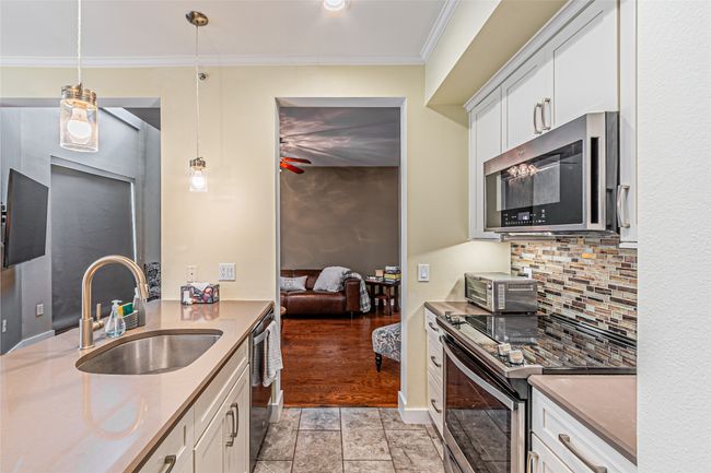 Kitchen with appliances with stainless steel finishes, backsplash, white cabinetry, crown molding, and light stone finish floors | Image 13