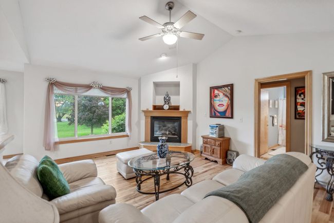 Living room with vaulted ceiling, ceiling fan, a glass covered fireplace, light wood-style floors, and baseboards | Image 4