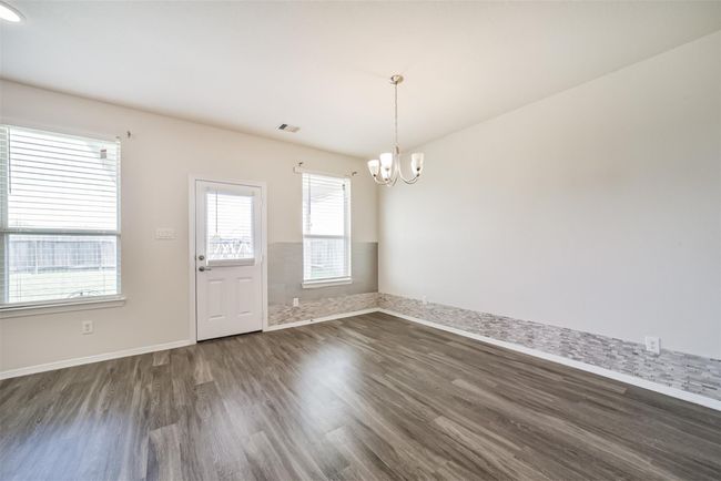 Bright and spacious room with large windows, modern light fixture, and wood-look flooring. Features a door leading outside and a stylish accent wall. Ideal for dining or living area. | Image 4