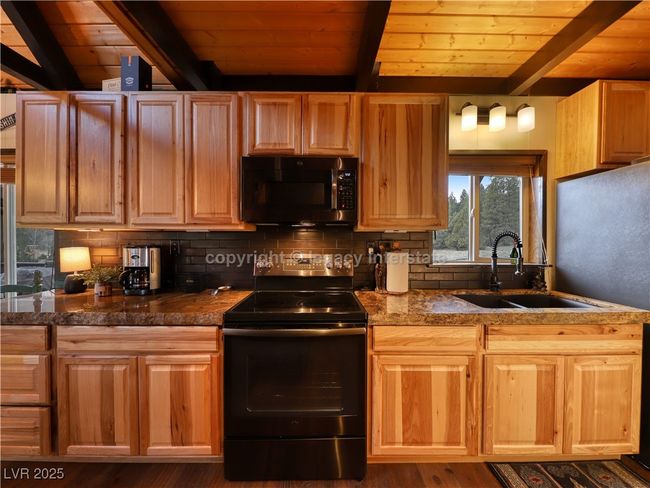 Kitchen featuring black electric range oven, beamed ceiling, wooden ceiling, a sink, and backsplash | Image 12