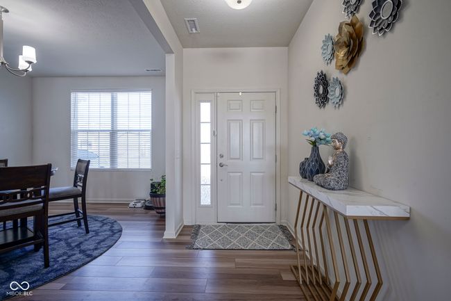foyer with a notable chandelier, wood finished floors, a textured ceiling, baseboards, and visible vents | Image 7