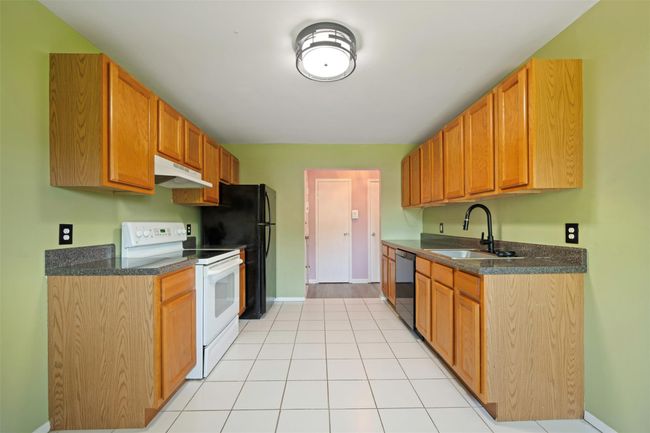 Kitchen with dark countertops, a sink, black dishwasher, under cabinet range hood, and white electric range | Image 6