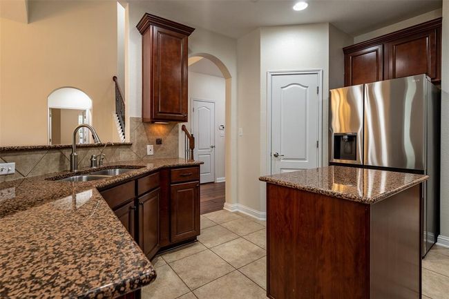 Kitchen with arched walkways, stainless steel fridge, dark stone counters, light tile patterned floors, and a center island | Image 8