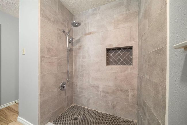 Beautifully updated walk-in shower features sleek oversized tile, a convenient handheld and rain shower fixture, and a recessed niche with designer accent tile. | Image 22
