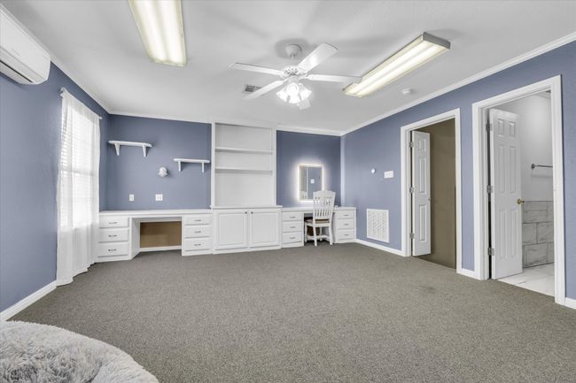 Carpeted bedroom featuring a wall mounted air conditioner, crown molding, baseboards, a ceiling fan, and ensuite bathroom | Image 25