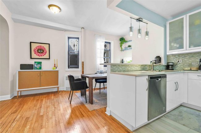 Kitchen featuring stainless steel dishwasher, a sink, white cabinetry, backsplash, and light wood-style floors | Image 5