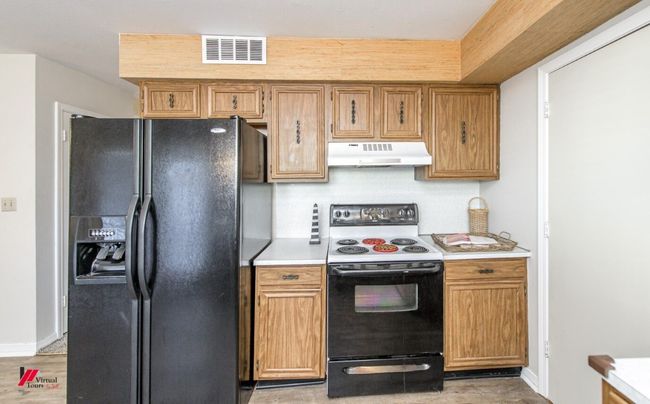 Kitchen with light countertops, black fridge, under cabinet range hood, electric range oven, and visible vents | Image 15