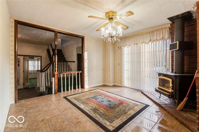 unfurnished room featuring a wood stove, stairway, wallpapered walls, tile patterned flooring, and a textured ceiling | Image 5