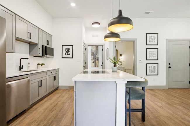 Kitchen featuring gray cabinets, a center island, light wood-style flooring, pendant lighting, and a breakfast bar area | Image 5