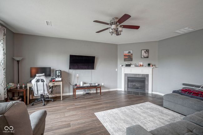 living room with a ceiling fan, wood finished floors, baseboards, and a tile fireplace | Image 17