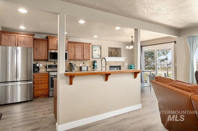 Kitchen featuring appliances with stainless steel finishes, a breakfast bar area, brown cabinets, light wood-style flooring, and tasteful backsplash | Image 6