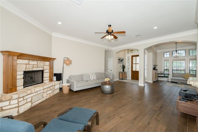 Living room with arched walkways, dark wood-type flooring, ceiling fan, a stone fireplace, and crown molding | Image 6