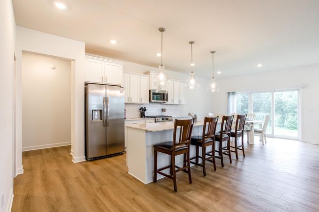 Bright and open kitchen featuring a large center island with seating, pendant lighting, quartz countertops, and stainless-steel appliances. | Image 5