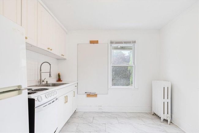 Kitchen featuring radiator heating unit, light tile patterned flooring, white cabinets, and white appliances | Image 16