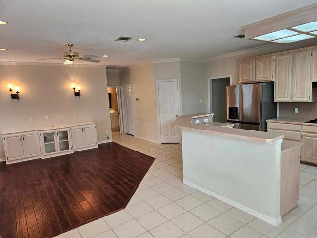 Kitchen featuring stainless steel fridge, ornamental molding, a ceiling fan, light countertops, and a kitchen island | Image 19