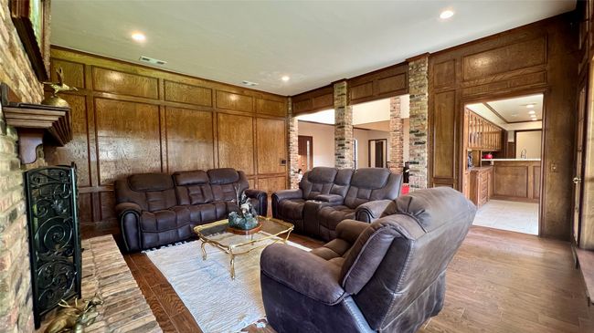 Living room with a decorative wall, recessed lighting, a fireplace, wood walls, and light wood finished floors | Image 4