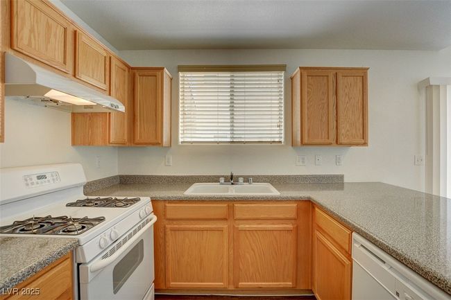 Kitchen featuring white appliances, under cabinet range hood, and a sink | Image 12