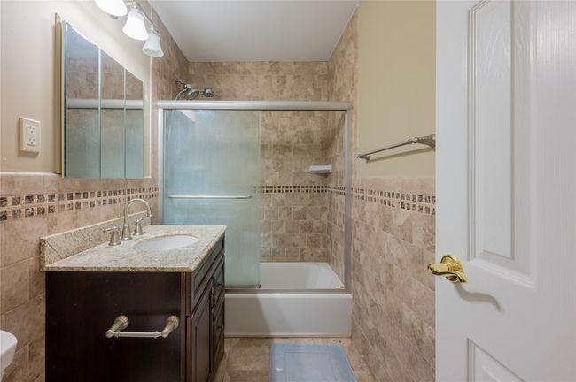 Full bathroom with shower / bath combination with glass door, vanity, a wainscoted wall, and tile walls | Image 8
