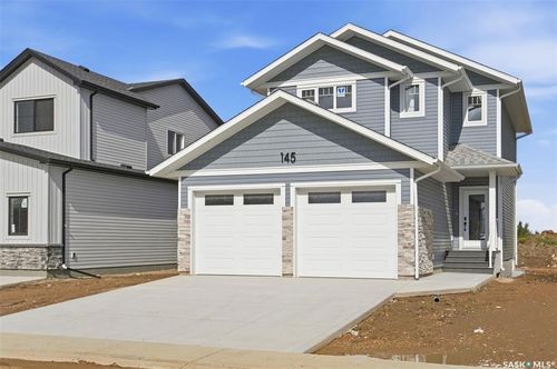 Two-story residence featuring blue siding, white trim accents, a two-car garage with transom windows, and a stone facade detail | Card Image