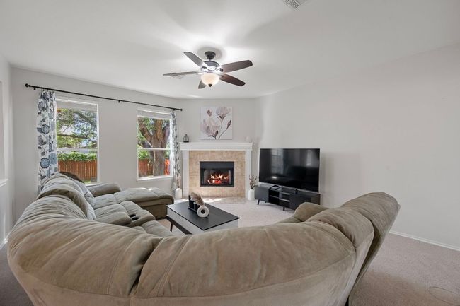 Carpeted living area featuring a ceiling fan, a tile fireplace, and baseboards | Image 10