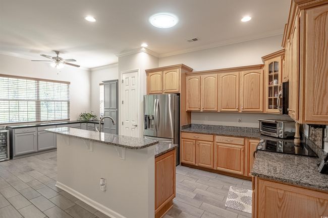 Kitchen with ceiling fan, stainless steel appliances, crown molding, an island with sink, and dark stone counters | Image 21
