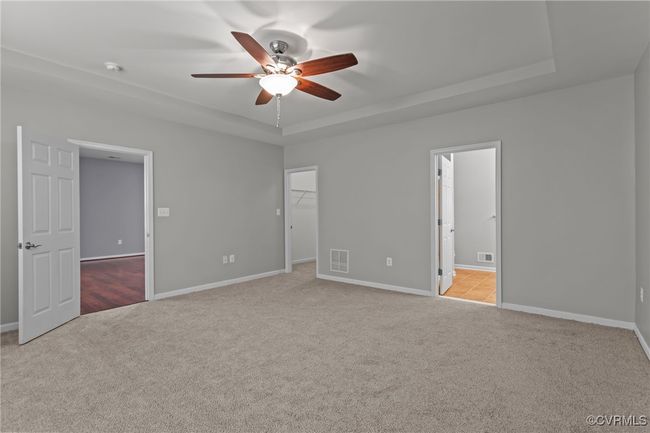 Unfurnished bedroom with carpet floors, a tray ceiling, a walk in closet, ensuite bathroom, and ceiling fan | Image 18