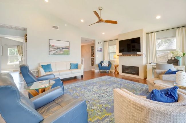 Living area featuring ceiling fan, a glass covered fireplace, lofted ceiling, wood finished floors, and recessed lighting | Image 6