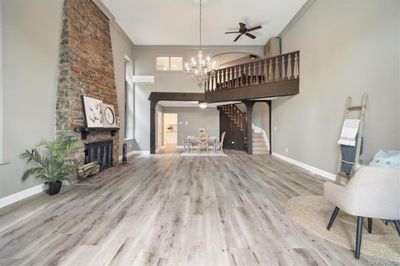 Living room with a stone fireplace, ceiling fan with notable chandelier, light hardwood / wood-style flooring, and crown molding | Image 3