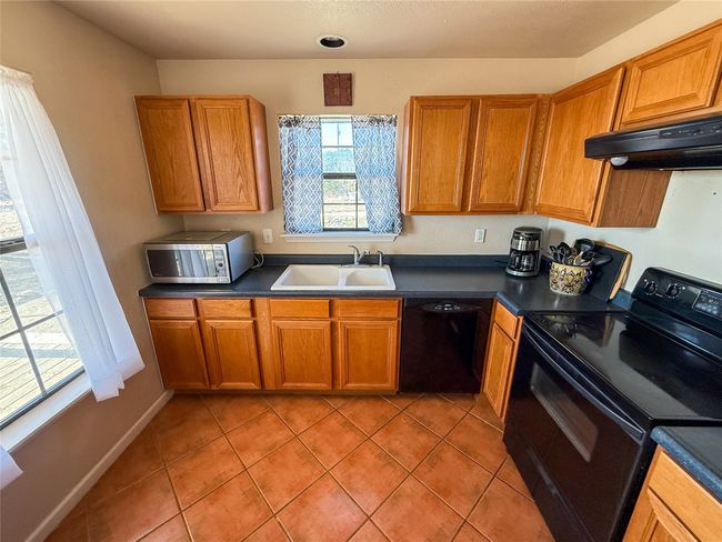 Kitchen with light tile patterned flooring, a sink, under cabinet range hood, dark countertops, and black appliances | Image 13