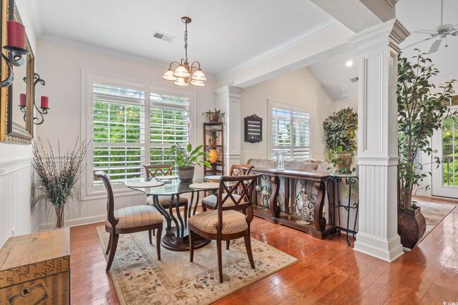 Dining room featuring decorative columns, wood-type flooring, wainscoting, crown molding, and ceiling fan | Image 22