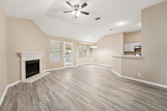 Unfurnished living room with a fireplace with raised hearth, a ceiling fan, light wood-style flooring, vaulted ceiling, and a chandelier | Image 6