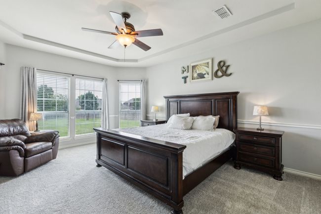 Primary bedroom on first floor with a tray ceiling, new carpet, ceiling fan, and ensuite bath with walk in closet | Image 17