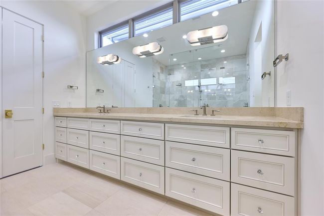 This spacious bathroom features a large double vanity with ample storage, elegant light fixtures, and a modern walk-in shower with glass doors. | Image 31