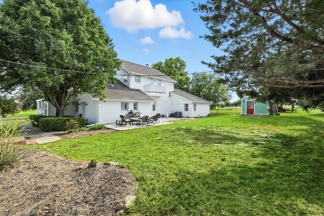 Back of house featuring a patio, a balcony, a lawn, a storage unit, and a shingled roof | Image 34