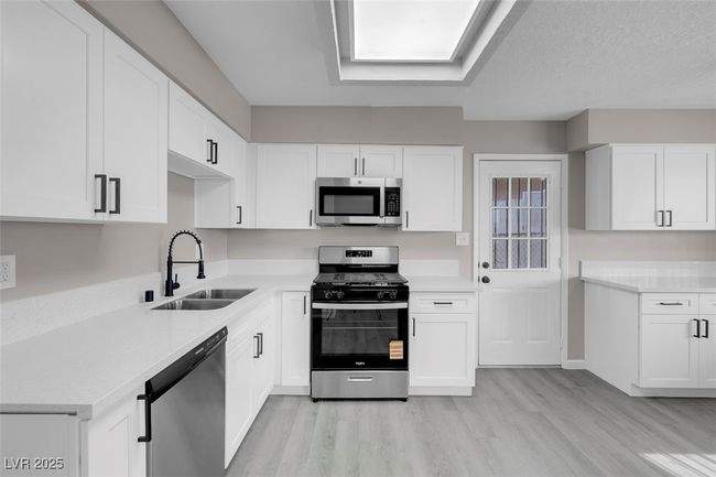 Kitchen with white cabinets, appliances with stainless steel finishes, a sink, and light wood-style floors | Image 17