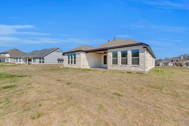 Rear view of house with stone siding, a patio area, a yard, and roof with shingles | Image 39