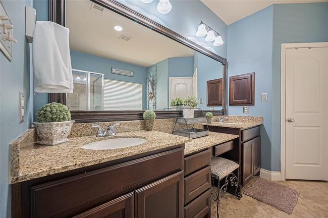 A closer look at the vanity reveals elegant granite countertops, nickel finishes, and a framed mirror that spans its length, complemented by updated lighting fixtures and ample cabinet and drawer storage. | Image 24