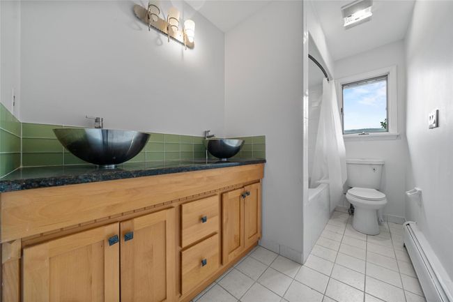 Bathroom with a baseboard heating unit, tile patterned flooring, shower / tub combo with curtain, backsplash, and vanity | Image 14